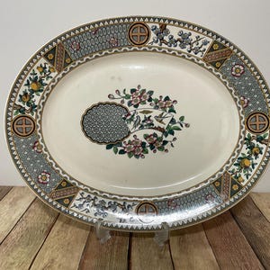 May include: A white oval serving platter with a decorative border featuring a repeating pattern of green, gold, and black. The centre of the platter features a floral design with birds and a geometric pattern.