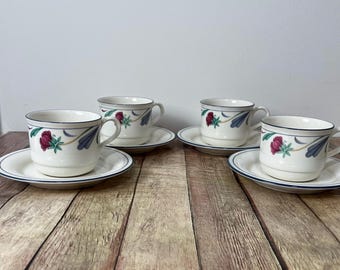 Puede incluir: Cuatro tazas y platillos a juego. Las tazas y los platillos son blancos con un ribete azul y un diseño floral con flores rojas y hojas azules. Las tazas tienen asas.