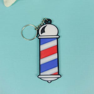 May include: A black and white barber pole keychain with red and blue stripes. The keychain has a silver ring.