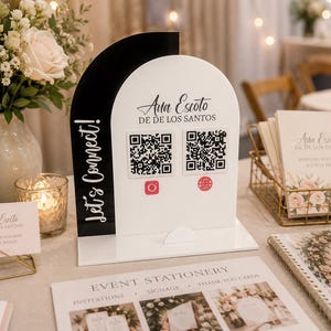 Op de afbeelding: Een zwart-wit acrylbord met een boogvormig ontwerp en de tekst Let's Connect! en Ana Escoto DE DE LOS SANTOS. Het bord bevat twee vierkante QR-codes met rode Instagram- en wereldbolpictogrammen op een platte, rechthoekige voet.