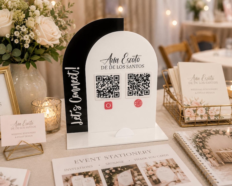Op de afbeelding: Een zwart-wit acrylbord met een boogvormig ontwerp en de tekst Let's Connect! en Ana Escoto DE DE LOS SANTOS. Het bord bevat twee vierkante QR-codes met rode Instagram- en wereldbolpictogrammen op een platte, rechthoekige voet.