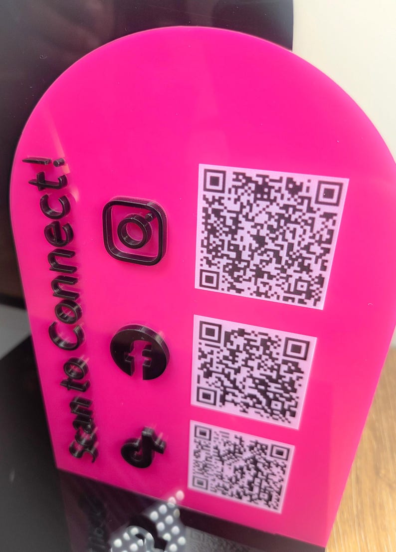 Op de afbeelding: Een felroze, boogvormig acrylbord met de zwarte tekst "Scan to Connect!" verticaal aan de linkerkant. Het bevat drie verhoogde zwarte social media iconen en drie bijbehorende witte QR-codes die aan de rechterkant zijn afgedrukt.