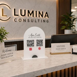 Op de afbeelding: Een wit boogvormig acrylbord met de tekst Ana Escoto DE DE LOS SANTOS, twee zwart-witte QR-codes en rode social media iconen. Het bord staat op een marmeren receptiebalie naast een transparant welkomstbord en een bezoekersbord.
