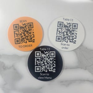 May include: Three round coasters with QR codes. One is orange with "SCAN TO ORDER", another is white with "Table 11 Scan to order", and the last is black with "Table 11 Scan to view Menu".