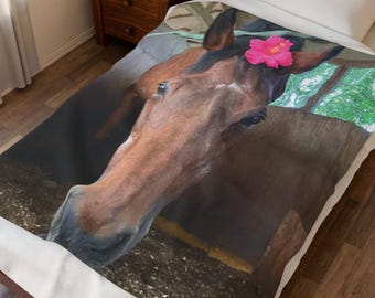 Puede incluir: Una manta con un caballo marrón con una flor rosa en la cabeza. La cabeza del caballo es la imagen central, con una vista de cerca de su cara y la flor. La manta está sobre una cama con un marco de madera.