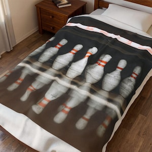 Könnte beinhalten: Eine Bowling-Decke mit einem sich wiederholenden Muster von Bowlingkegeln mit roten Streifen auf schwarzem Hintergrund. Die Decke hat einen weißen Rand und ist über ein Bett drapiert.