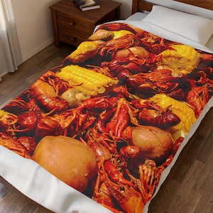 May include: A blanket featuring a vibrant image of a crawfish boil. The design showcases a close-up of cooked crawfish, corn on the cob, and potatoes. The blanket is spread out on a bed with a white sheet and pillow.