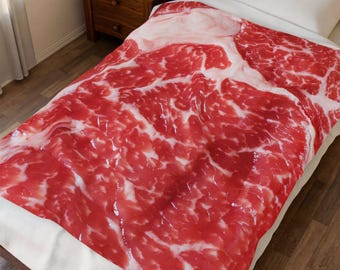 Puede incluir: Una colcha con una impresión realista de carne de res cruda. El patrón rojo y blanco imita la apariencia de un gran corte de carne, con vetas y textura detalladas. La colcha está sobre una cama con una almohada blanca.