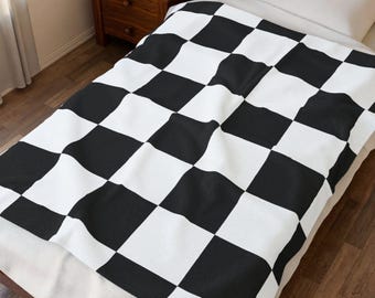 Puede incluir: Una manta rectangular con un patrón de cuadros blancos y negros repetitivos. La manta está extendida sobre una cama, cubriendo el colchón y la almohada, mostrando un diseño de cuadrícula de alto contraste con bloques cuadrados uniformes.