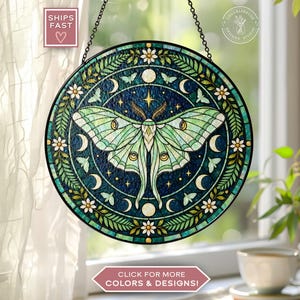 May include: A circular stained glass suncatcher featuring a large light green luna moth at the center. The design includes a dark blue background with white crescent moons, stars, small moths, and a border of white flowers and green leaves.