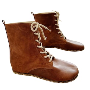 May include: A pair of brown leather ankle boots with white laces. The boots have a rounded toe and a stitched seam around the sole.