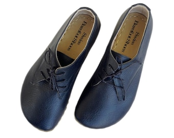 May include: A pair of black leather lace-up shoes with a rounded toe. The shoes have a brown leather insole with the text "Swiss Barefoot Shoes" printed on them.