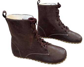 May include: A pair of brown leather ankle boots with white stitching and laces. The boots have a flat sole.