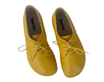 May include: A pair of yellow leather lace-up shoes with the word "Swiss" printed on the inside of each shoe.