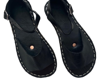 May include: A pair of black leather sandals with a buckle closure and a stitched edge. The sandals have a simple design and are made of high-quality leather.