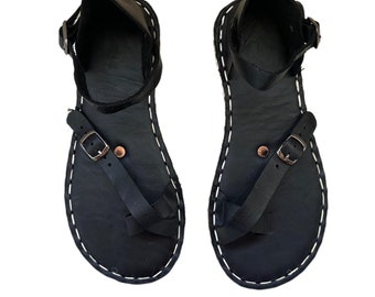 May include: A pair of black leather sandals with a buckle closure and white stitching around the edges.