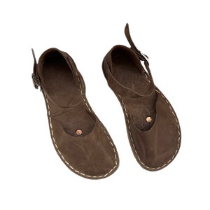 May include: A pair of brown leather sandals with a buckle closure and a white stitch detail around the sole.