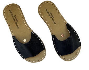 May include: A pair of black leather slides with a brown leather sole. The soles have a white stitch around the edge and the text "Swiss Handmade Shoes" is printed on the sole.