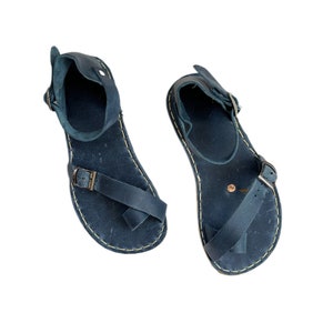 Pode incluir: Um par de sandálias de couro azul escuro com fivelas. As sandálias têm um design simples e são feitas de couro de alta qualidade.