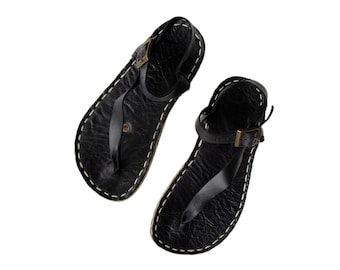 May include: A pair of black leather sandals with a simple design and adjustable ankle straps. The sandals have a stitched edge and a textured leather upper.
