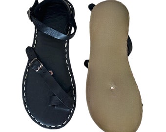 May include: A pair of black leather sandals with a single strap across the foot and an adjustable buckle closure. The sandals have a brown leather insole and a stitched edge.