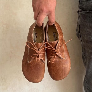 Op de afbeelding: Een paar bruine leren veterschoenen met het woord "SWISS" gedrukt aan de binnenkant van elke schoen.