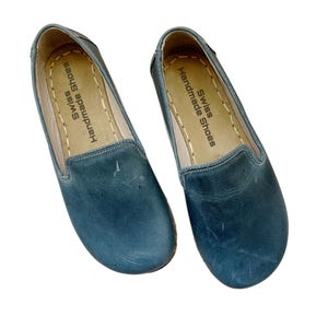 Könnte beinhalten: Ein Paar blaue Lederschuhe zum Hineinschlüpfen mit einer braunen Ledersohle. Die Innensohle trägt den Aufdruck "Swiss Handmade Shoes".
