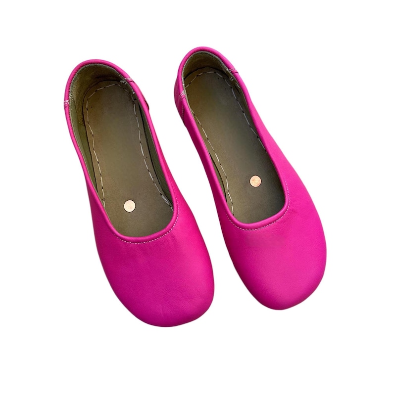 May include: A pair of bright pink ballet flats. The shoes have a rounded toe and a flat sole. The interior is a muted green color with a small, round, beige accent. The shoes are made of a smooth material.