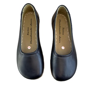 May include: A pair of black leather ballet flats. The shoes have a rounded toe and a stitched sole. The inner sole is tan with the text "Swiss Handmade shoes".