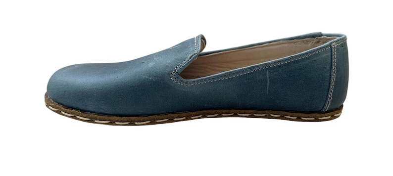 May include: A pair of blue leather slip-on shoes with a white stitch detail around the sole.