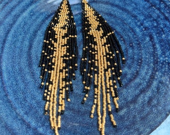 May include: A pair of long, black and gold beaded earrings. The earrings are made of small beads that are strung together in a cascading pattern. The earrings are about 4 inches long.