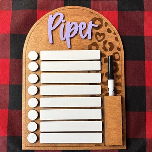 Peut inclure: Un tableau d'effacement à sec en bois avec un motif léopard et le nom "Piper" écrit en violet. Le tableau comporte 10 lignes vierges pour écrire et un emplacement pour un marqueur effaçable à sec.