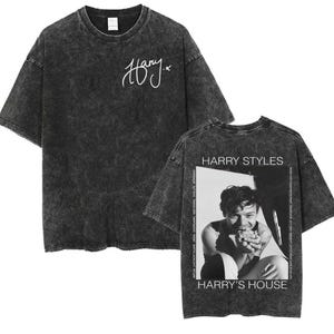 Puede incluir: Camiseta negra con lavado ácido y firma blanca en la parte delantera. La parte trasera muestra una foto en blanco y negro de Harry Styles, con el texto "HARRY STYLES" y "HARRY'S HOUSE".