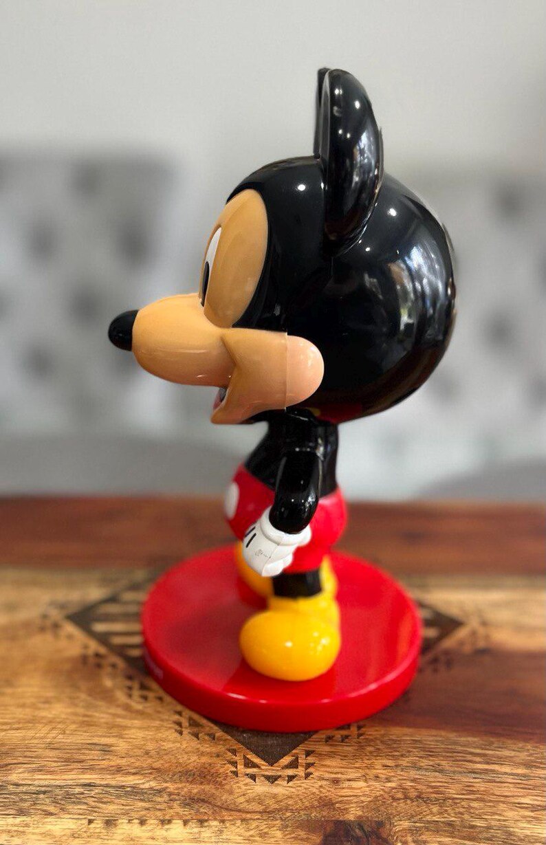 K&ouml;nnte beinhalten: Eine schwarze und rote Mickey Mouse Figur mit gelbem Sockel. Die Figur steht auf einem roten Sockel mit einem schwarz-wei&szlig;en Muster.