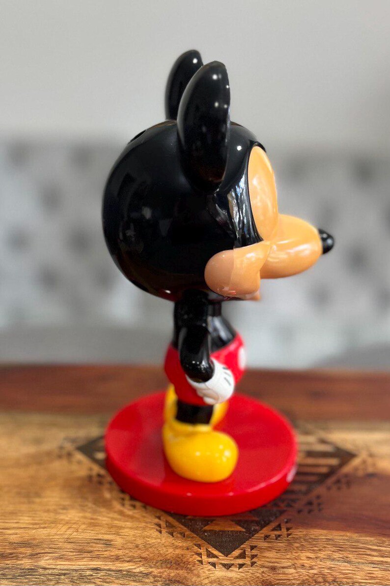 K&ouml;nnte beinhalten: Eine schwarze und rote Mickey Mouse Figur mit gl&auml;nzender Oberfl&auml;che. Die Figur steht auf einem roten Sockel.