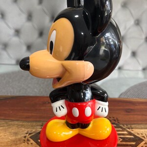 K&ouml;nnte beinhalten: Eine schwarze und rote Mickey Mouse Figur mit gelben Schuhen. Die Figur steht auf einem roten Sockel mit dem Text "Walt Disney World Resort".