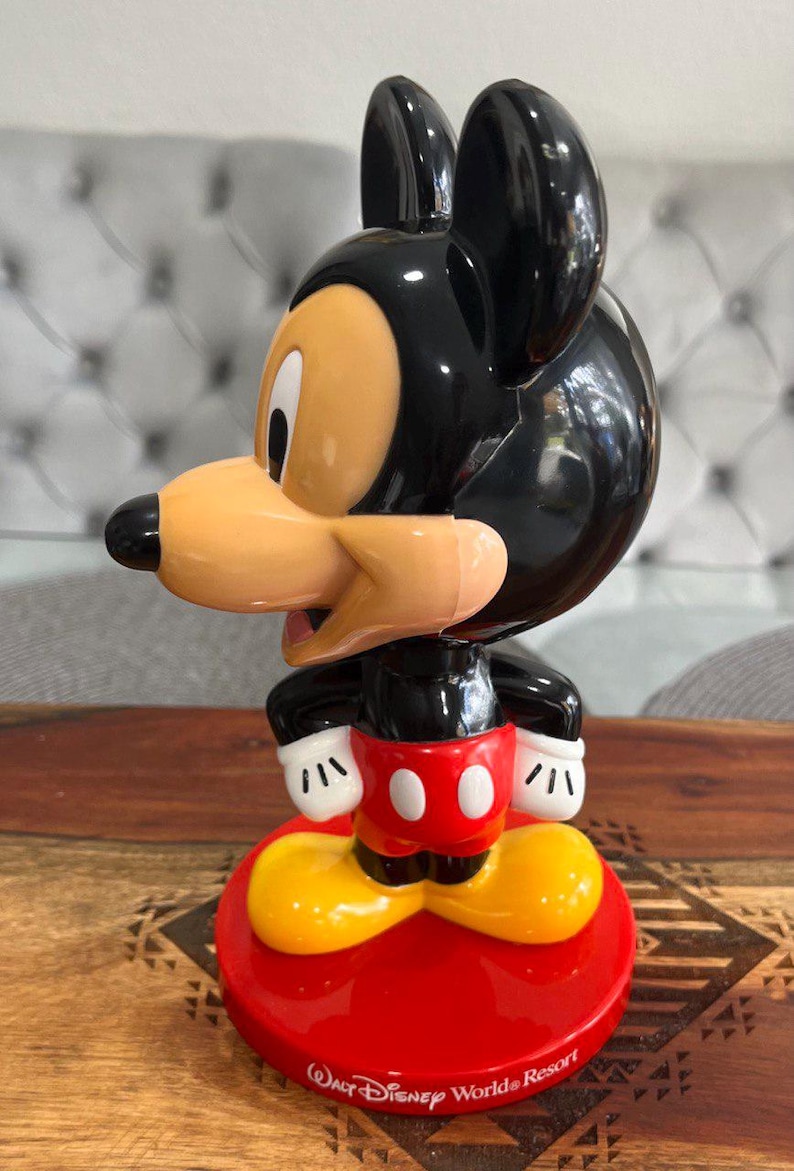 K&ouml;nnte beinhalten: Eine schwarze und rote Mickey Mouse Figur mit gelben Schuhen. Die Figur steht auf einem roten Sockel mit dem Text "Walt Disney World Resort".