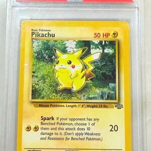 May include: A graded 1999 Pok&eacute;mon Jungle Pikachu card. The card features a yellow Pikachu illustration with the text "Pikachu" and "50 HP". The card is in a protective case with a label that reads "#60 MINT 9".
