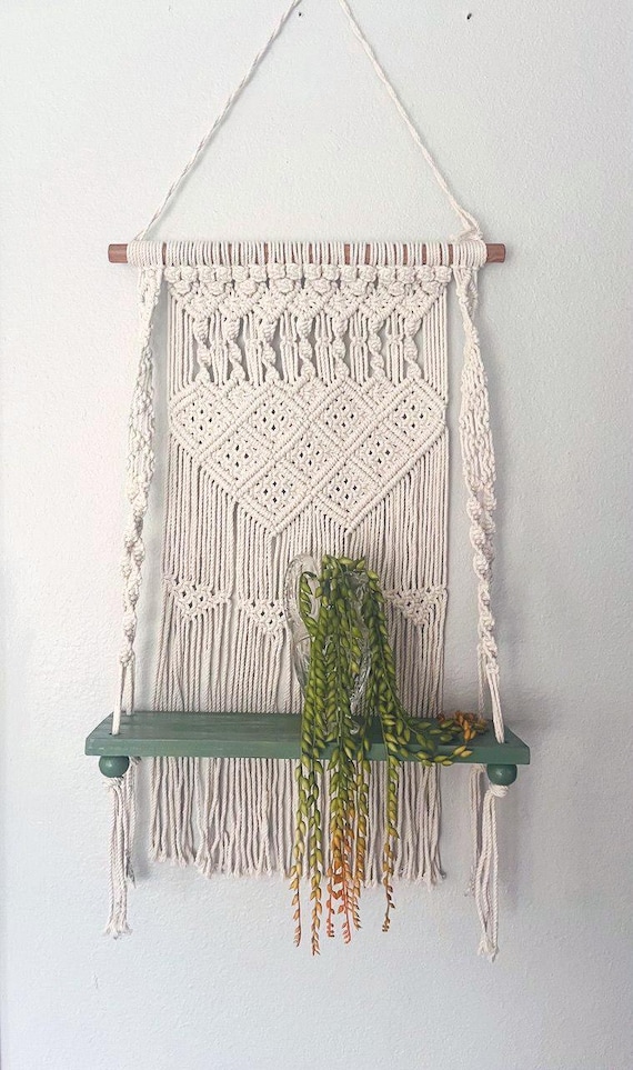 Combining a macrame textile with an integrated green wood shelf is a genuinely functional-meets-artisan hybrid — you get storage AND wall art in one handmade object.