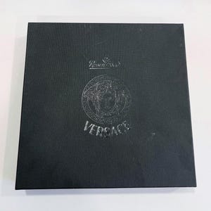 May include: A black square box with the Versace logo embossed on the front. The logo features a Medusa head and the word "VERSACE" below it. The box also has the "Rosenthal" logo at the top.