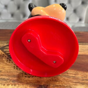 K&ouml;nnte beinhalten: Rote Plastikbasis mit einem Mickey-Mouse-Kopfdesign. Die Basis hat zwei Schrauben auf der Unterseite und der Text "Walt Disney World" ist seitlich aufgedruckt.