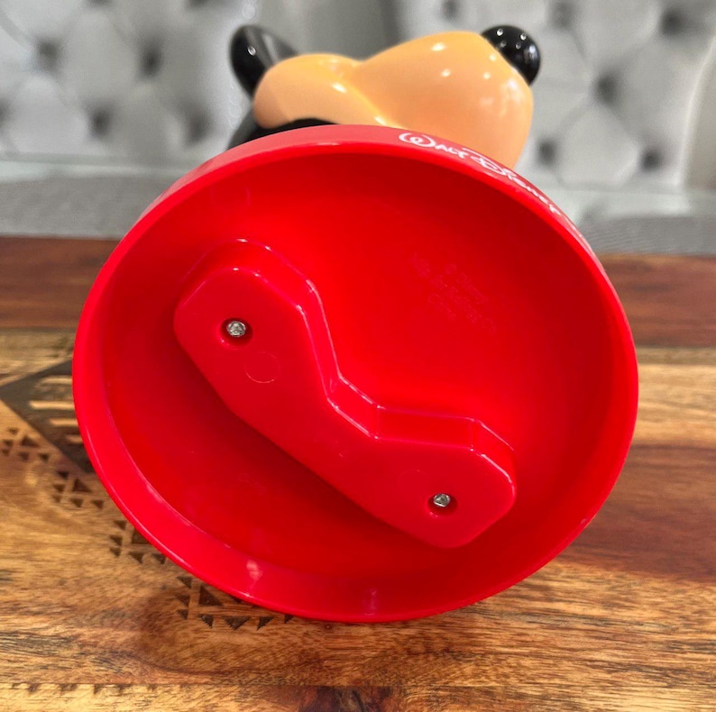 K&ouml;nnte beinhalten: Rote Plastikbasis mit einem Mickey-Mouse-Kopfdesign. Die Basis hat zwei Schrauben auf der Unterseite und der Text "Walt Disney World" ist seitlich aufgedruckt.