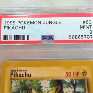May include: A graded Pok&eacute;mon card featuring Pikachu from the 1999 Jungle set. The card is encased in a clear plastic holder with a red label displaying "1999 POKEMON JUNGLE PIKACHU" and a PSA grade of "9". The card is labeled "#60 MINT".