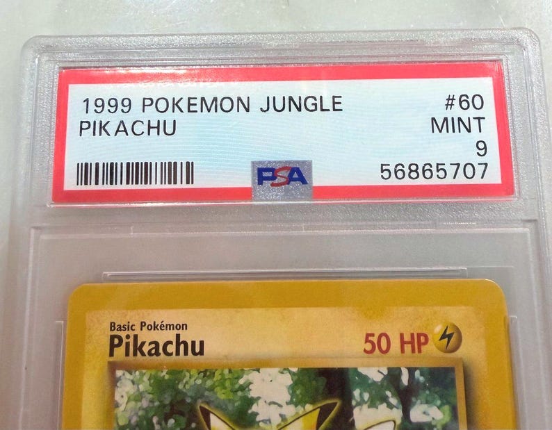 May include: A graded Pok&eacute;mon card featuring Pikachu from the 1999 Jungle set. The card is encased in a clear plastic holder with a red label displaying "1999 POKEMON JUNGLE PIKACHU" and a PSA grade of "9". The card is labeled "#60 MINT".