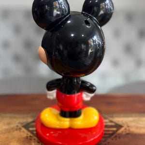 K&ouml;nnte beinhalten: Eine schwarze und rote Mickey Mouse Figur mit gelben Schuhen. Die Figur steht auf einem roten Sockel.