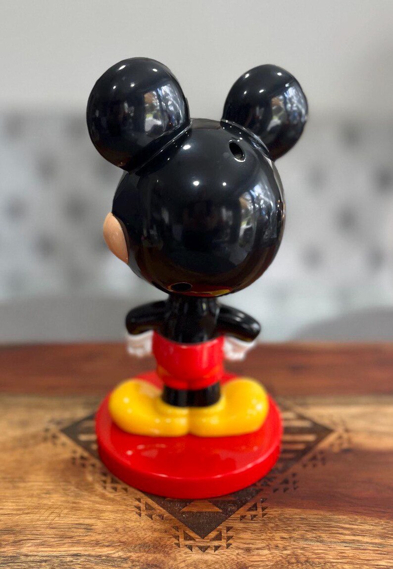 K&ouml;nnte beinhalten: Eine schwarze und rote Mickey Mouse Figur mit gelben Schuhen. Die Figur steht auf einem roten Sockel.