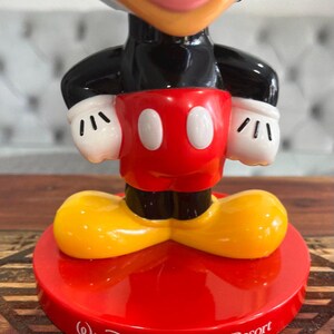 K&ouml;nnte beinhalten: Eine rote, gelbe und schwarze Mickey Mouse Figur mit einem roten Sockel. Der Sockel tr&auml;gt den Schriftzug "Walt Disney World&reg; Resort".