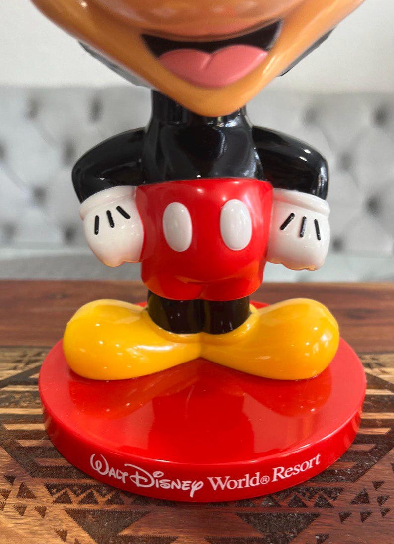 K&ouml;nnte beinhalten: Eine rote, gelbe und schwarze Mickey Mouse Figur mit einem roten Sockel. Der Sockel tr&auml;gt den Schriftzug "Walt Disney World&reg; Resort".