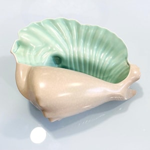 Może przedstawiać: Ceramiczna miska w kształcie muszli z jasnozielonym wnętrzem i beżowym zewnętrzem. Miska ma teksturowany, żebrowany wzór wewnątrz i gładki, zakrzywiony kształt na zewnątrz. Miska jest zaprojektowana tak, aby przypominać muszlę.