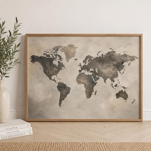 May include: A framed world map art print with a watercolour effect. The map features continents in shades of grey and brown against a neutral background. The wooden frame adds a natural touch. Decorative books and a vase with greenery are in the foreground.
